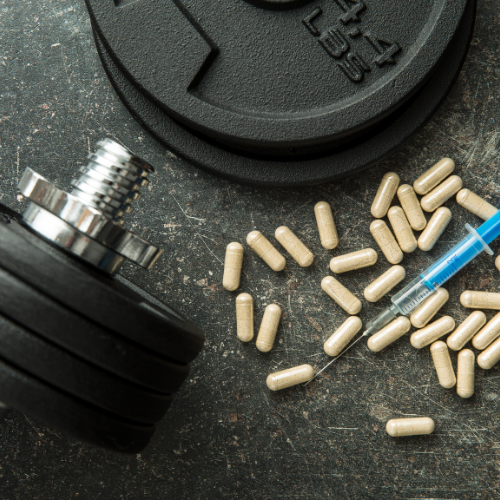 Halteres, cápsulas e seringa sobre superfície escura, representando suplementação, hormônios e relação entre exercício e saúde metabólica.