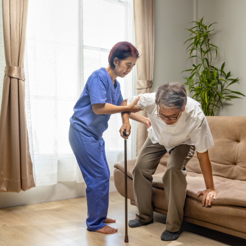 Profissional de saúde auxiliando pessoa idosa a se levantar do sofá, representando cuidados com mobilidade e sarcopenia.